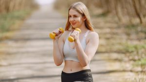Fit woman lifting dumbbells on a sunny day, embracing a healthy outdoor workout.