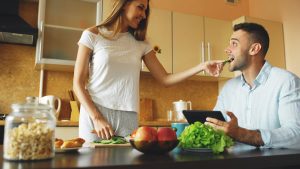 Attractive couple chatting in the kitchen early morning. Beautiful woman feed her husband while cooking breakfast at home